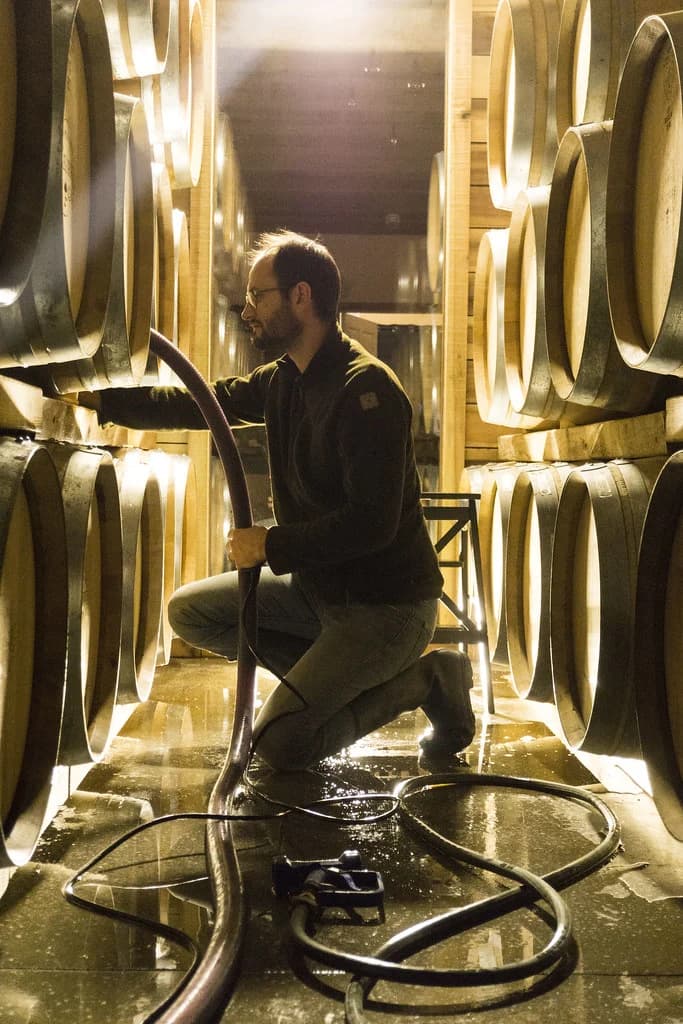 Sébastien LeSeurre kneeling in the barrel cellar, filling a barrel by hand